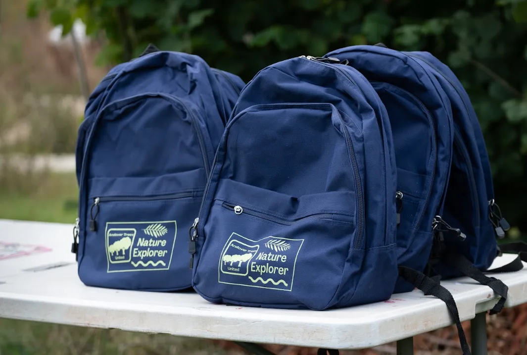 Navy rucksacks printed with the Andover Trees United logo and the words Nature Explorer, lined up on a white folding table outdoors